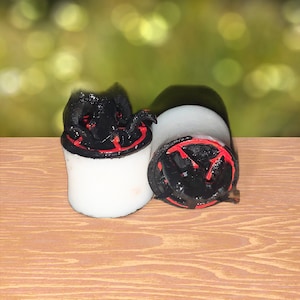 Pode incluir: Dois expansores de orelha pretos e vermelhos com um design detalhado. Os expansores são de acrílico e têm uma base branca.