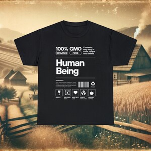 May include: Black t-shirt with a white graphic design that reads "100% GMO FREE ORGANIC Human Being". The graphic also includes a barcode, a recycle symbol, and icons for fragile, emotional being, made with love, handle with care, and requires coffee.