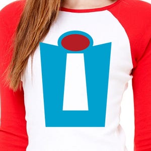 Puede incluir: Una camiseta de b&eacute;isbol blanca y roja con un gr&aacute;fico azul y blanco de una puerta con un c&iacute;rculo rojo en la parte superior. El gr&aacute;fico recuerda a la puerta de la pel&iacute;cula Up.