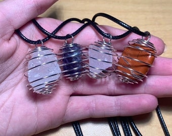 May include: Four crystal necklaces with wire cages. The crystals are clear quartz, amethyst, clear quartz, and red jasper. The necklaces have black cords.