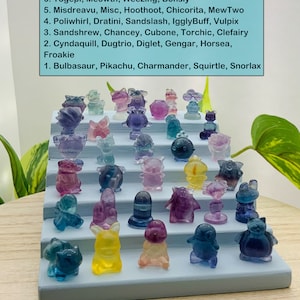 May include: A collection of colorful Pokemon figurines arranged on a blue wooden shelf. The figurines are made of clear plastic and feature different Pokemon characters, including Bulbasaur, Pikachu, Charmander, Squirtle, Snorlax, Growlith, Wigglytuff, Rhydon, Togepi, Meowth, Weezing, Bonsly, Misdreavu, Misc, Hoothoot, Chicorita, MewTwo, Poliwhirl, Dratini, Sandslash, IgglyBuff, Vulpix, Sandshrew, Chancey, Cubone, Torchic, Clefairy, Cyndaquill, Dugtrio, Diglet, Gengar, Horsea, and Froakie.