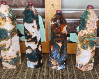 May include: Four colorful, multi-faceted, polished agate crystal points with red tops. The points are arranged in a row on a wooden surface.