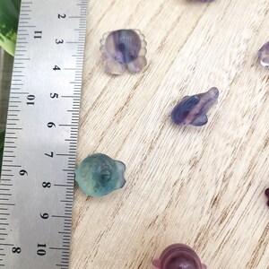 May include: A collection of small, carved fluorite animal figurines in shades of purple, blue, and green. The figurines include a crab, fish, and frog. A ruler with centimeter markings is in the frame, showing the size of the figurines.