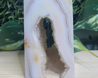 May include: White agate crystal with a natural opening revealing a cluster of smaller crystals. The crystal is shaped like a house and is approximately 2 inches tall.