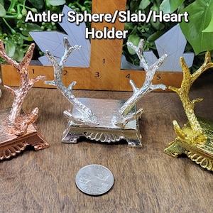 May include: Three antler sphere/slab/heart holders in different finishes: copper, silver, and gold. Each holder features a pair of antlers on a square base with decorative detailing.