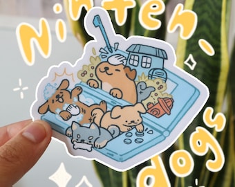 May include: A sticker featuring a cartoon illustration of four dogs playing on a Nintendo DS. The dogs are a brown and white dog, a gray and white dog, a brown dog, and a white dog. The sticker is on a white background with the words "Ninten-dogs" in yellow.