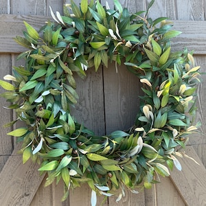 May include: A green olive branch wreath with small brown olives. The wreath is hanging on a wooden door.