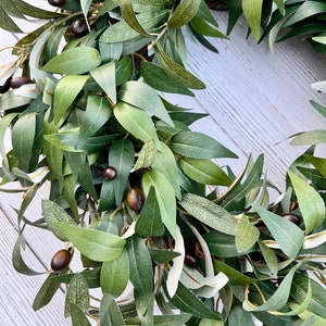 May include: A green olive branch wreath with brown olives. The wreath is made of artificial leaves and is perfect for adding a touch of nature to your home decor.