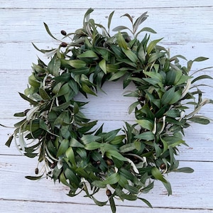 May include: A green olive branch wreath with brown olives. The wreath is made of artificial leaves and is perfect for decorating a home or office.