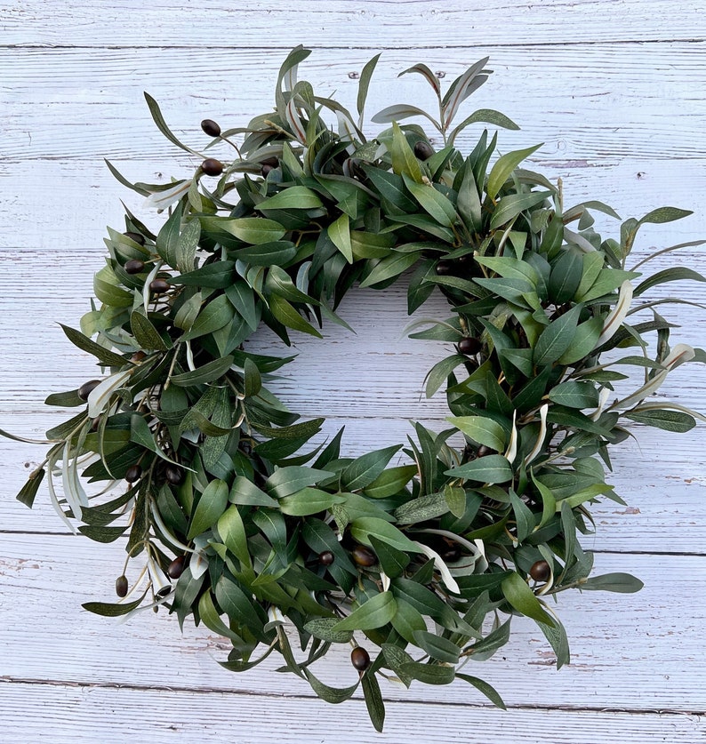 May include: A green olive branch wreath with brown olives. The wreath is made of artificial leaves and is perfect for decorating a home or office.