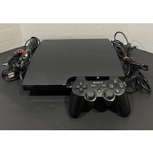 Op de afbeelding: Een zwarte Sony PlayStation 3 console met een zwarte draadloze controller. De console is aangesloten op een stroomkabel en een AV-kabel.