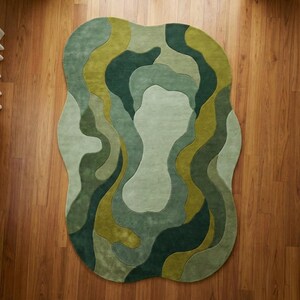 Organic modern hand-tufted wool rug in layered green abstract shapes with sculptural edges, styled in a warm minimalist living room.