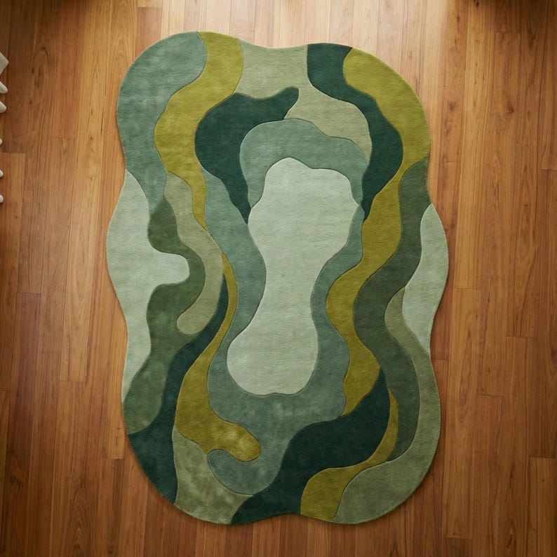 Organic modern hand-tufted wool rug in layered green abstract shapes with sculptural edges, styled in a warm minimalist living room.