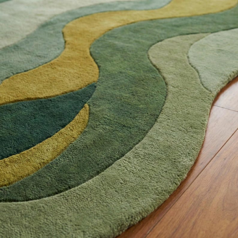 May include: A green area rug with a wavy design. The rug features shades of green and olive, creating a layered effect. The rug is placed on a wooden floor.