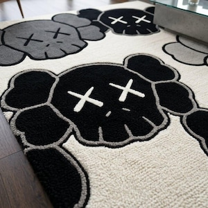Close-up corner of a premium hand-tufted New Zealand wool rug featuring a black KAWS-inspired character head with white X eyes, showing the dense cream wool pile, deep black outlines, and high-low hand-carved textures on a dark hardwood floor.