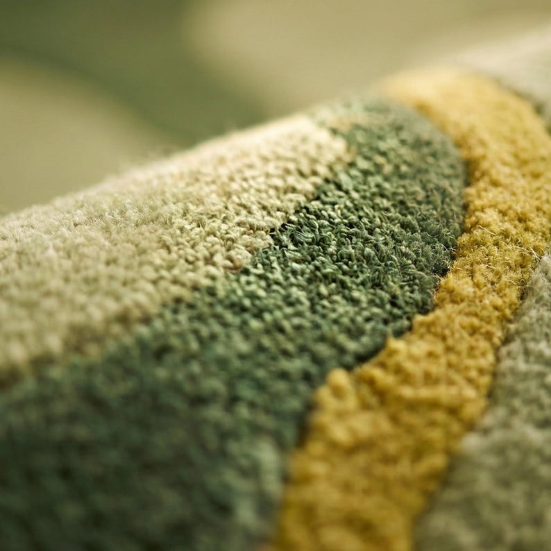 May include: Close-up of a textured rug with a pattern of curved stripes. The rug features shades of green, beige, and yellow. The fibers are tightly woven, creating a soft, plush appearance. The rug's design adds a touch of color and texture to any space.