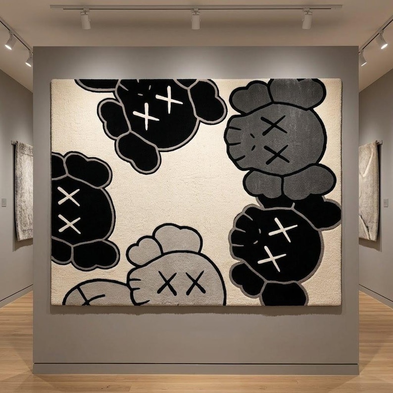 A square hand-tufted pop art character wool rug in black, grey, and cream displayed vertically as textile wall art under gallery spot lighting, showcasing the symmetrical placement of the cartoon character heads.