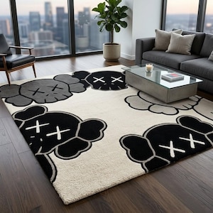 ​A large rectangular greyscale pop-art character wool area rug styled under a wooden coffee table, surrounded by a grey sofa and a brown leather lounge chair in a warm, wood-paneled mid-century modern living room.