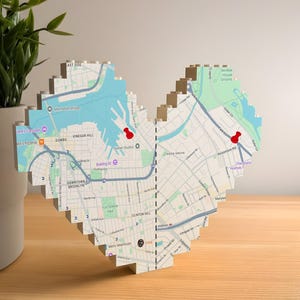 Könnte beinhalten: Eine herzförmige Karte von Brooklyn, New York, mit roten Pins, die Standorte markieren. Die Karte besteht aus ineinandergreifenden Blöcken mit einem pixeligen Design. Die Karte enthält Straßennamen, Gewässer und Sehenswürdigkeiten.