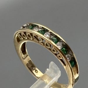 Peut inclure: Une bague en or avec un sertissage rail alternant des émeraudes vertes et des diamants blancs transparents ronds. Le côté de l'anneau présente un motif ajouré de cercles répétitifs, et l'intérieur est marqué du poinçon 10K.