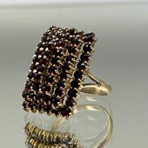 Op de afbeelding: Een gouden ring met een brede band bezet met meerdere rijen kleine, donkerrode granaatsteen.