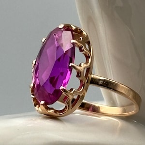 May include: A gold ring with a large, oval-shaped, purple gemstone set in a delicate, ornate setting.