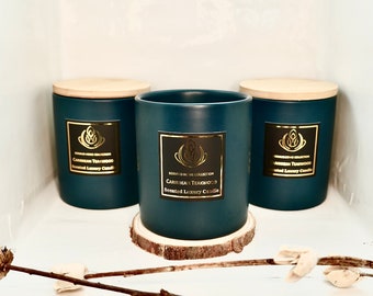 Puede incluir: Tres velas azul verdoso con tapas de madera. Las velas están etiquetadas como "Caribbean Teakwood Scented Luxury Candle".