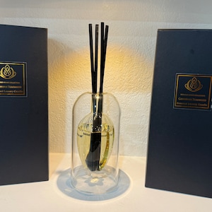 May include: Two black boxes with gold lettering that reads "Caribbean Teakwood Scented Luxury Candles" and a glass diffuser with black reeds.