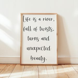 May include: A framed print with a white background and black text that reads "Life is a river, full of twists, turns and unexpected beauty."