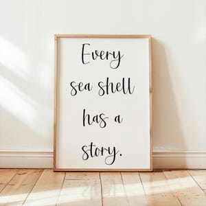 May include: A framed print with the text "Every sea shell has a story." The print is on a white background with black text and is framed in a light wood frame.