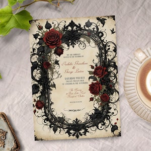 May include: A gothic wedding invitation with a black and white ornate frame with red roses. The text reads "You are cordially invited to the wedding of Isabella Grantham & George Linton Saturday 9th July Twenty Twenty Four at 3 o'clock in the afternoon The Ceremony at Great Lake Road Mansfield, Ontario Reception to follow"