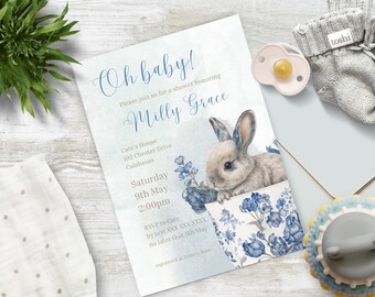 May include: A blue and white baby shower invitation with a watercolour illustration of a bunny rabbit holding blue flowers. The invitation reads "Oh baby! Please join us for a shower honouring Milly Grace. Cate's House, 102 Chester Drive, Calabasas. Saturday, 9th May, 2:00pm. RSVP to Cate by text XXX XXX XXXX no later than 5th May. Registered at Pottery Barn."