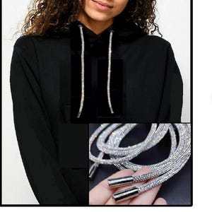 May include: Black hoodie with long, silver rhinestone drawstring cords. Close-up of the cords, which are made of small, sparkling rhinestones.
