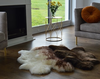 May include: Two sheepskin rugs, one white and one brown, are laid out on a hardwood floor. The rugs are in a living room setting with a couch and a gold end table.