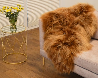 May include: A brown sheepskin rug with long, fluffy fur. The rug is draped over a light-colored sofa.