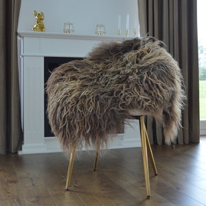 May include: A chair with a sheepskin seat and gold-colored legs. The sheepskin is a mix of brown and beige tones, creating a textured appearance. The chair's legs are slender and angled, adding a touch of elegance to the design.