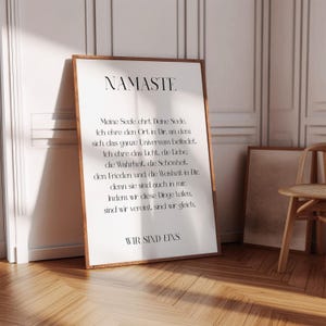 Puede incluir: Un p&oacute;ster de pared imprimible en blanco y negro con la palabra "Namaste" en letras grandes en la parte superior. El p&oacute;ster presenta un poema en alem&aacute;n sobre el significado de la palabra "Namaste".