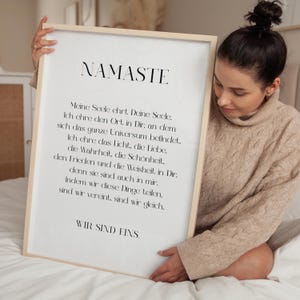 Puede incluir: Una impresi&oacute;n enmarcada blanca con la palabra "Namaste" en texto negro. La impresi&oacute;n presenta un poema en alem&aacute;n sobre el significado de la palabra "Namaste".