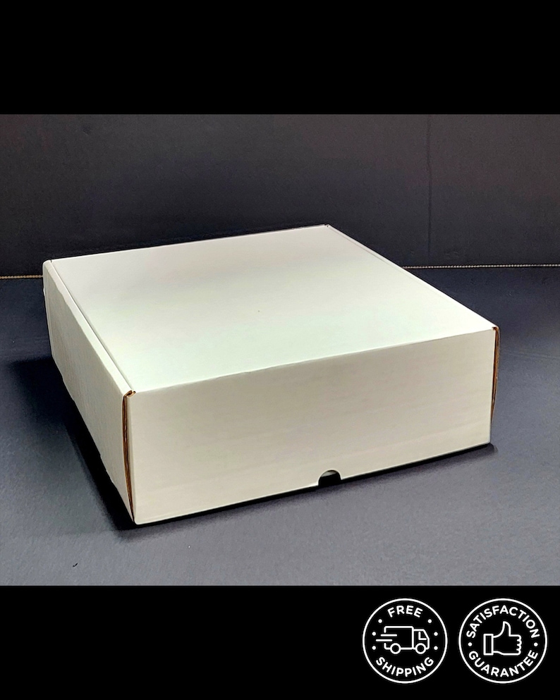 May include: A square white cardboard shipping box with a flat top and a front-facing tab closure. The box is constructed from plain white material and features clean, straight edges, presenting a simple and functional design for packaging items.