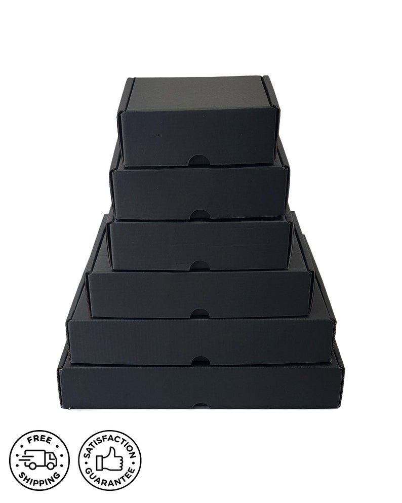 May include: A stack of six black cardboard boxes of varying sizes, arranged from largest at the bottom to smallest at the top. Each box has a lid with a small tab for opening. The boxes are on a white background. Two circular icons are in the lower left corner.