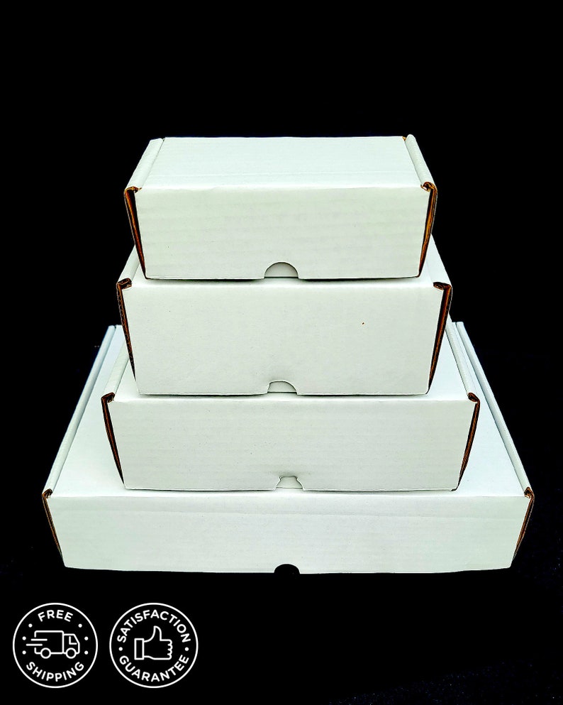 May include: A stack of four white rectangular cardboard shipping boxes arranged in a pyramid shape, with the smallest box on top and the largest on the bottom. Each box features a front-facing tab closure and a clean, matte white exterior finish.
