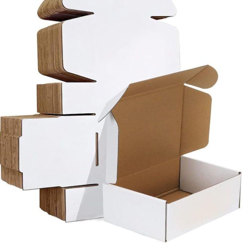 May include: A stack of flat, unfolded white cardboard shipping boxes alongside one fully assembled rectangular box. The boxes feature a clean white exterior finish with a natural brown corrugated cardboard interior visible on the edges and inside.