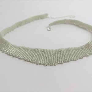 May include: A delicate, light green beaded necklace with a fringe design. The necklace is made of small, uniform beads and has a simple silver clasp.