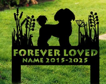 May include: Black metal garden stake featuring a silhouette of a dog within a decorative border of plants. The text "FOREVER LOVED" and a name and dates are displayed below the dog silhouette. The stake is placed in a grassy area with flowers in the background.
