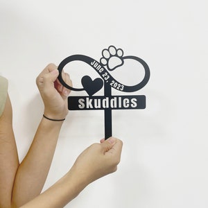 May include: Black metal infinity symbol with a paw print and heart, with the text "June 23, 2023" and "Skuddles" on a white background.