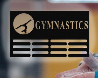 May include: A black sign with the word "GYMNASTICS" in gold lettering. A silhouette of a gymnast performing a handstand on a bar is in a circle on the left side of the sign. There are five horizontal lines below the word "GYMNASTICS".