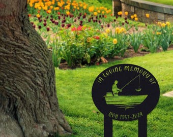May include: Black metal memorial garden stake with a silhouette of a person fishing in a boat. The text "In loving memory of" and "1953-2024" is included.