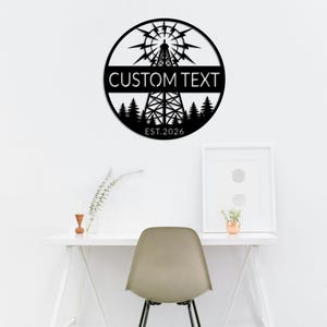 Peut inclure: Décoration murale en métal noir de forme circulaire, représentant un chevalet de forage stylisé. Le texte "CUSTOM TEXT" est centré, avec "EST.2026" en dessous. Le design comprend une silhouette de forêt.