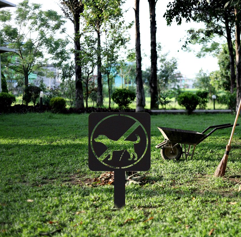 May include: Black metal sign with a white circle and a diagonal line through it. Inside the circle is a silhouette of a dog. The sign is on a black metal stake and is in a grassy area.