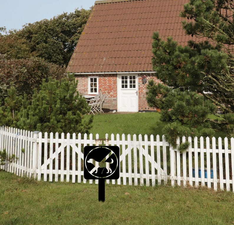 May include: A black metal sign with a white silhouette of a dog with a diagonal line through it. The sign is mounted on a black metal post and is in front of a white picket fence. The sign reads "No Dogs Allowed".